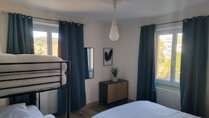A bedroom with bunk beds, a bedside table with a plant, a mirror, and a window with curtains. - Bright ground-floor apartment with garden. (Gérardmer)