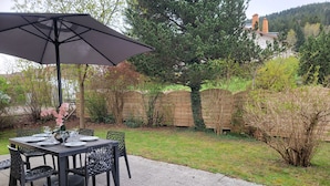 An outdoor patio with a table set for dining, surrounded by a garden with a wooden fence and trees. - Bright ground-floor apartment with garden. (Gérardmer)