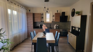 A modern kitchen with wooden cabinets, a dining table with chairs, and a coffee machine. - Bright ground-floor apartment with garden. (Gérardmer)