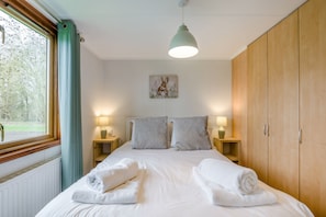 Ein Schlafzimmer mit einem Bett, zwei Nachttischen mit Lampen, einem Holzschrank, einem Fenster mit Vorhängen und einem Bild an der Wand.