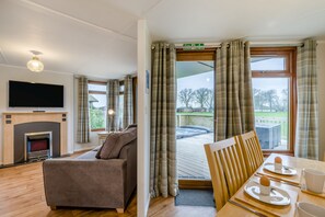 Ein Wohnzimmer mit einer Couch, einem Flachbildfernseher, einem Kamin und einem Balkon mit Frühstückstisch.
