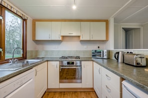 A compact kitchen with white cabinets, a built-in oven, a gas stove, a toaster, and a kettle. - Athelington lodge - Beech  - sleeps 6 guests  in 2 bedrooms (Eye)