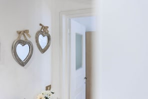 A bathroom with two heart-shaped mirrors on the wall, a door leading to another room, and a vase with flowers on the counter.