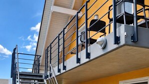 Un edificio de varios pisos con fachada amarilla, una escalera metálica y una cámara de seguridad.