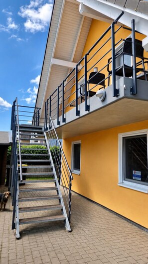 A multi-story building with a yellow exterior, a metal staircase, and a security camera.