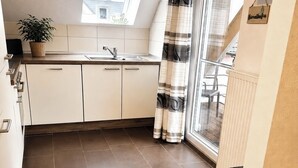 Una cocina moderna con tragaluz, armarios blancos, un cubo de basura negro y una cortina a rayas.