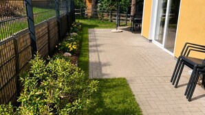 En terrasse med græsplæne, hegn og en bygning med en glasdør.