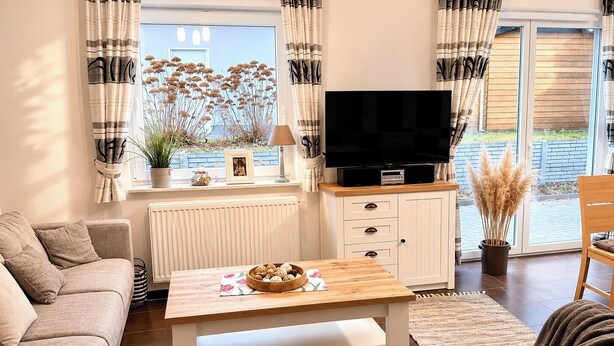 En stue med sofa, sofabord, fjernsyn og et vindue med gardiner.
