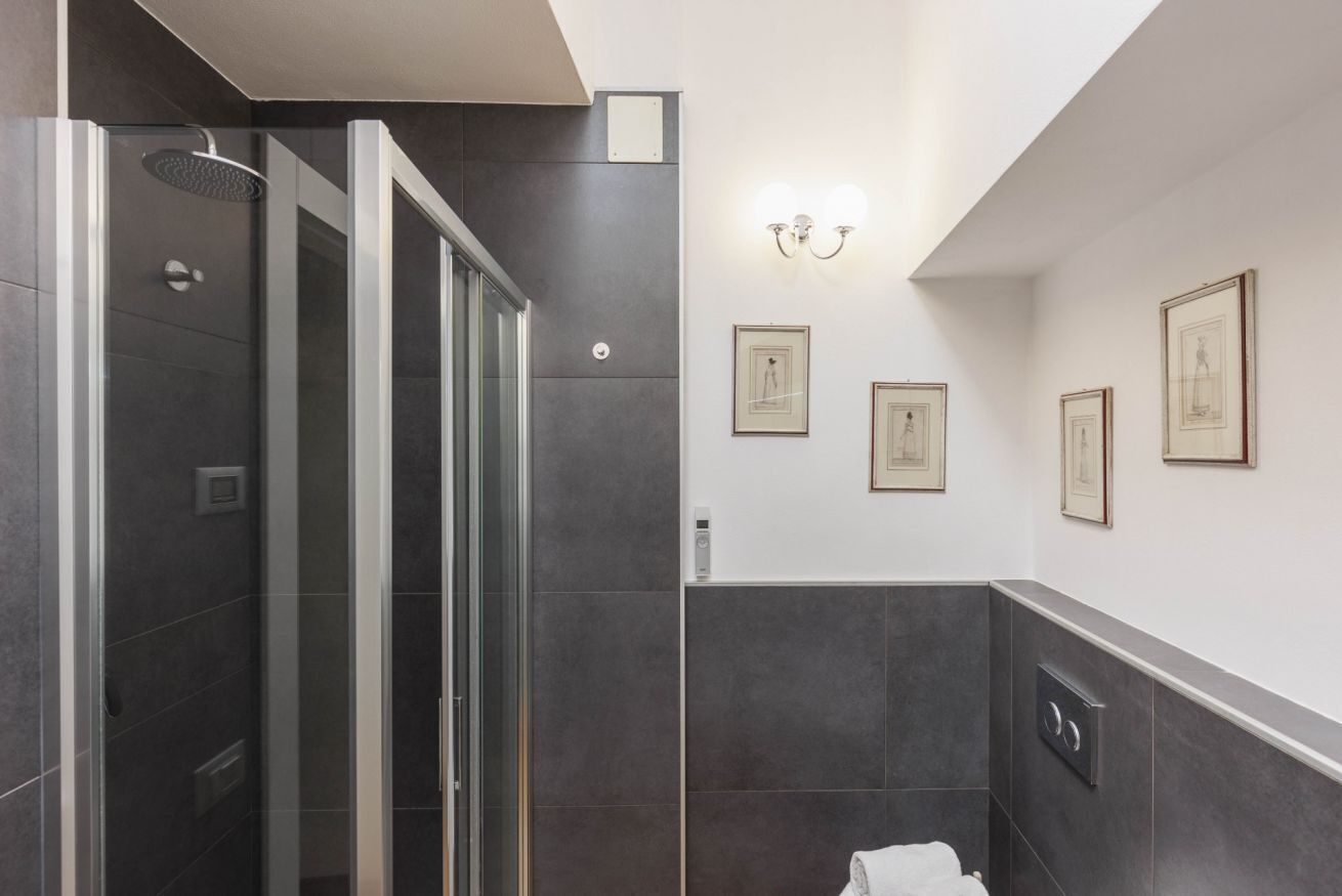 A modern bathroom with a glass-enclosed shower, dark tiles, and framed artwork on the walls.