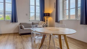 Una habitación moderna con una mesa redonda de madera, sillas traslúcidas, un sofá gris y una lámpara.