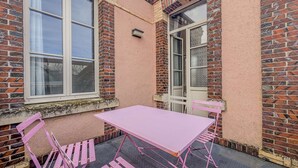 Un pequeño patio al aire libre con una mesa y sillas rosas, un muro de ladrillo y una ventana.