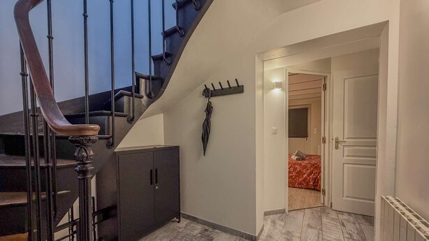 Una escalera con barandilla oscura y balaustrada de madera, que lleva a una habitación con cama y armario.