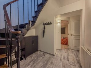 Un escalier doté d’une main courante sombre et d’une balustrade en bois, menant à une pièce où se trouvent un lit et une armoire.