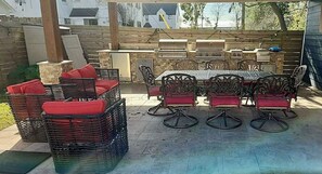 An outdoor patio with wicker chairs and a table, barbecue grills, and a stone wall in the background. - Lucky House 2 Tranquility in the Middle of Houston (Houston)