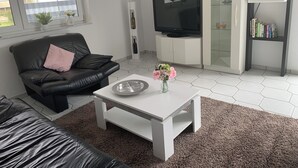 A modern living room with a black leather sofa, a white coffee table, a TV, and a bookshelf. - Feel good for 1-4 people at Casa Berg in Spiesen-Elversberg (Spiesen-Elversberg)