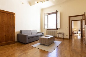 Een woonkamer met een grijze bank, een houten salontafel en een groot raam met zonwering.