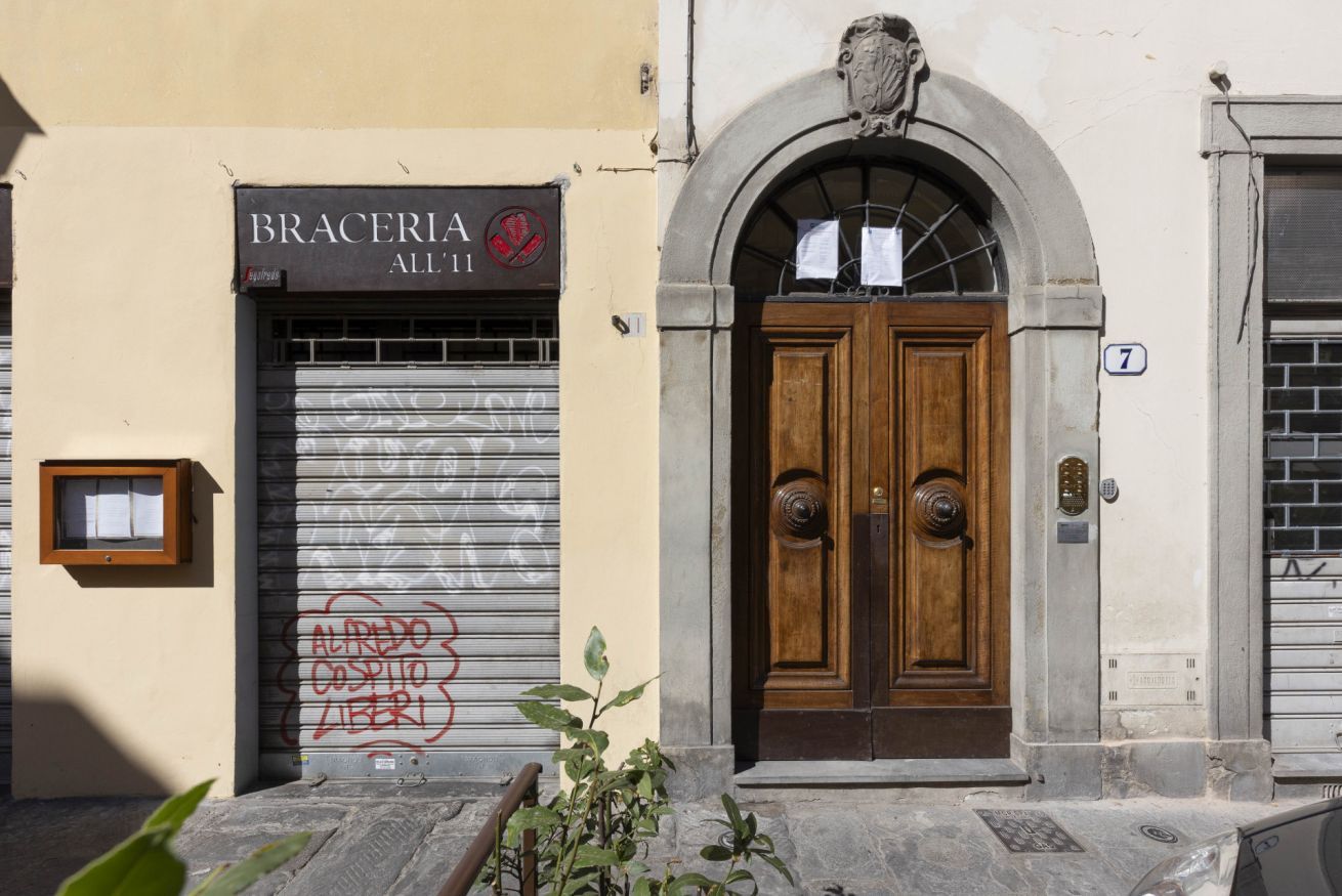 Un bâtiment avec une porte fermée par un volet, une porte double en bois et une enseigne indiquant « BRACERIA ALL'11 ».
