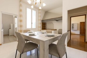 A dining area with a wooden table set for four, surrounded by chairs. There is a kitchen visible in the background with a built-in shelf. - Santo Spirito Huge Apartment (Florence)