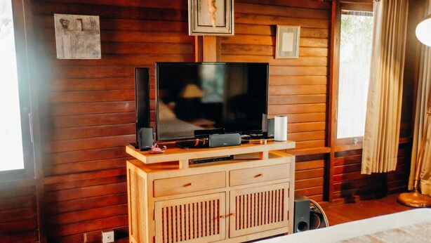 Una habitación con paneles de madera, un televisor sobre un mueble de madera, una cama y una ventana con cortinas.