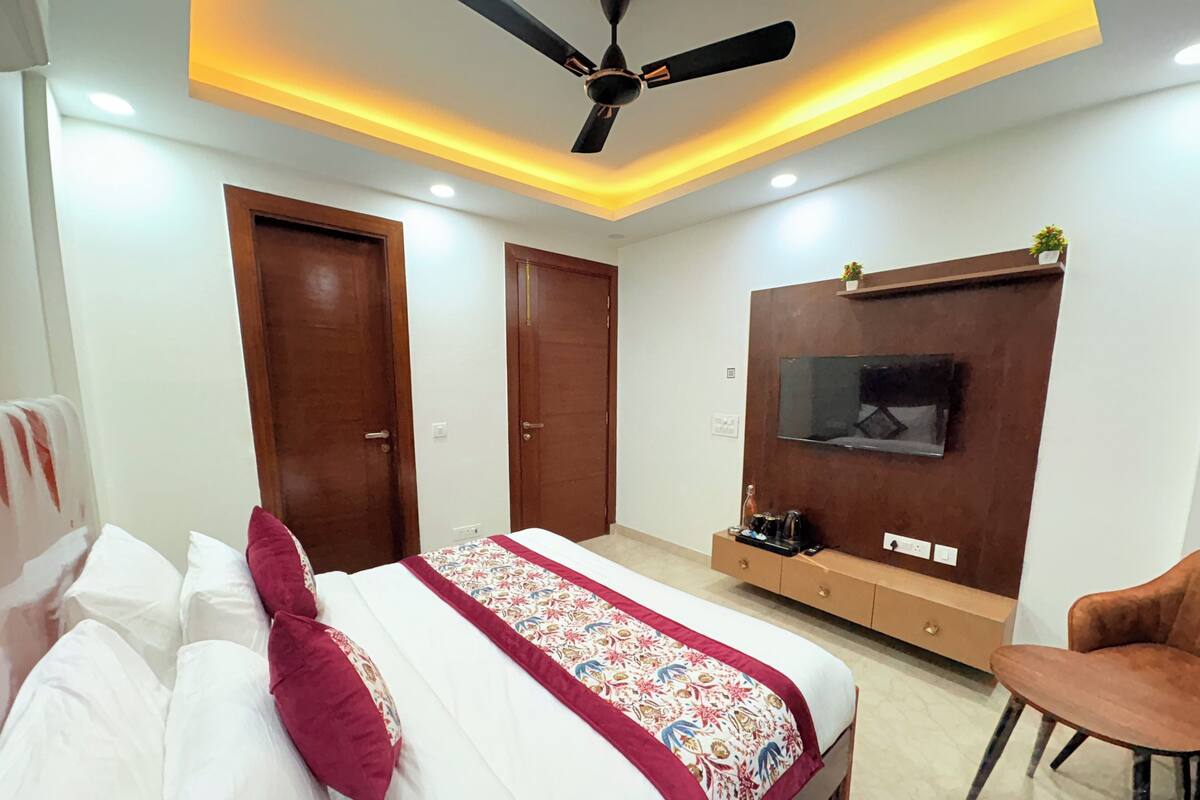 Une chambre à coucher comprenant un lit, un ventilateur de plafond, un téléviseur fixé au mur et un petit meuble.