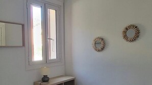 Quarto com cama, cadeira, mesa de cabeceira, janela e duas decorações na parede.