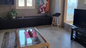 Uma sala de estar moderna com uma mesa de centro de vidro, um sofá preto, um quadro abstrato colorido e uma TV em um suporte.