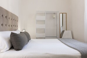 A neatly made bed with a tufted headboard, a bedside table with a lamp, and a walk-in closet with shelves and a mirror. - Santo Spirito Living (Firenze)