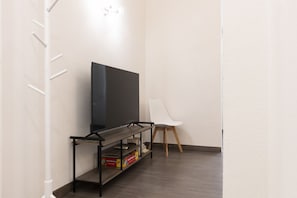 A modern living room with a flat-screen TV on a black TV stand, a white chair, and a white wall. - Santo Spirito Living (Firenze)