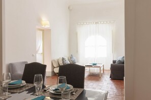 Zona pranzo con tavolo apparecchiato per quattro persone, un divano e una finestra con tende.