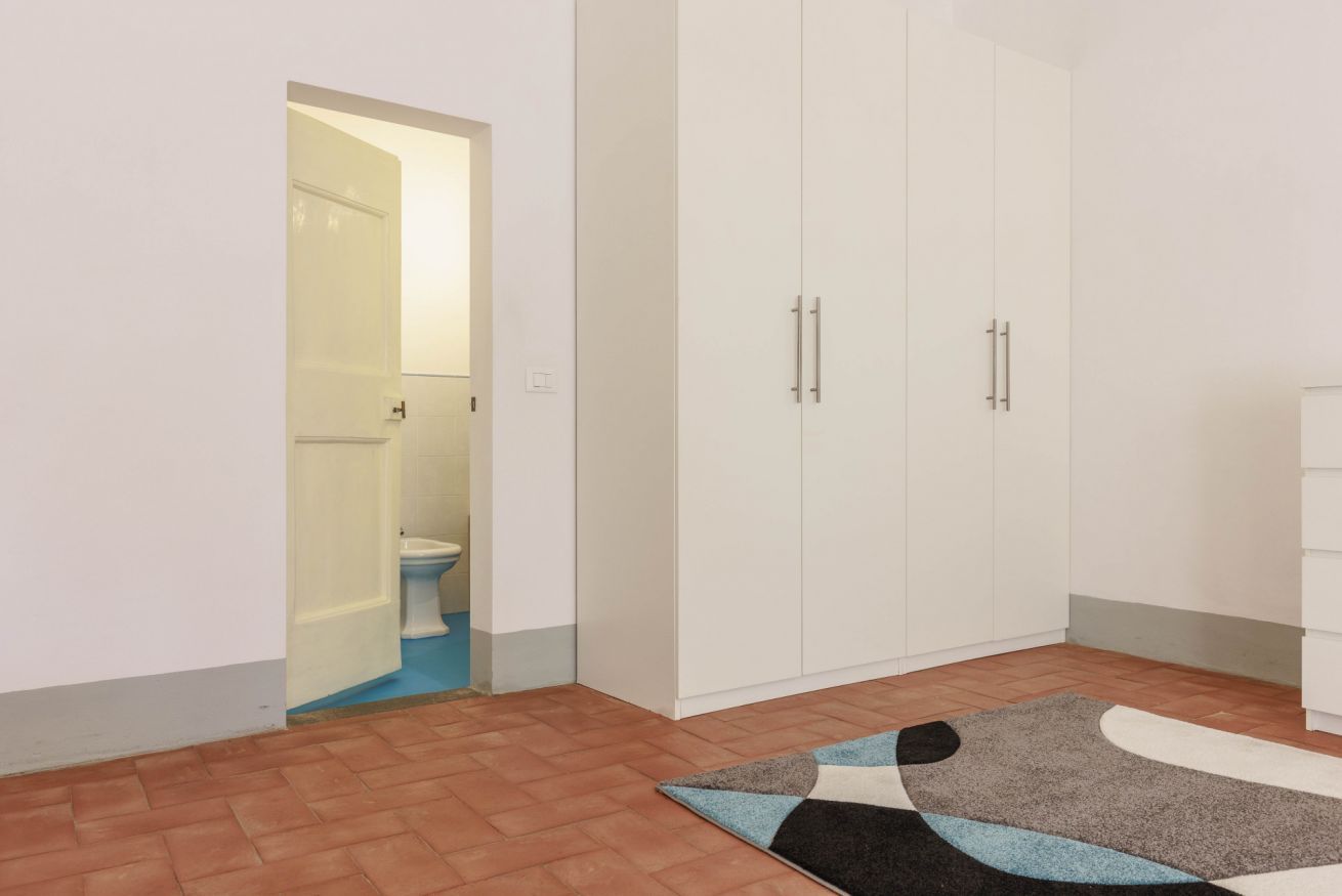 Ein Zimmer mit offener Badezimmertür, einem weißen Kleiderschrank und einem gemusterten Teppich.