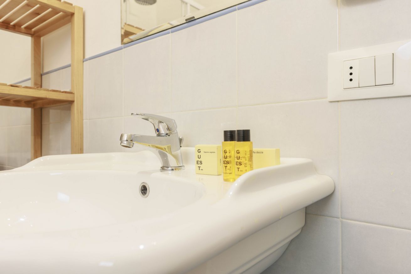 A bathroom sink with a mirror above it, a wooden shelf, and toiletries on the sink.