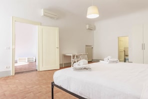 Una camera d'albergo con un letto, una scrivania e una sedia. Sul letto ci sono degli asciugamani e a parete uno specchio.