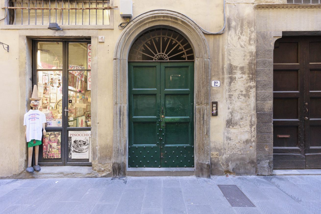 Une porte verte surmontée d’une arche décorative, un petit balcon avec une balustrade et une enseigne au-dessus de la porte.