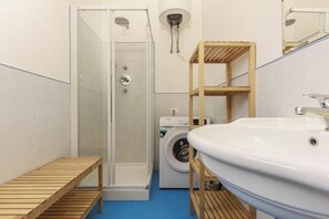Une salle de bain avec une douche à parois de verre, un lave-linge et une étagère en bois.