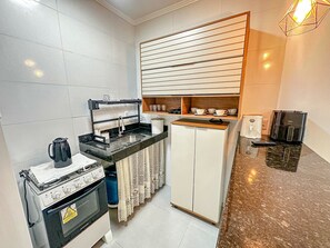 A compact kitchen with a gas stove, a sink, a small refrigerator, and a coffee maker. - Condomíno American Praia  (Porto Seguro)