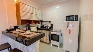 A compact kitchen with a gas stove, a microwave, and a refrigerator. There is a coffee maker and a kettle on the counter. - Condomíno American Praia  (Porto Seguro)