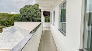 A narrow balcony with a metal roof, a glass door, and a view of greenery. - Condomíno American Praia (Porto Seguro)
