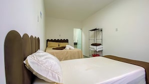 Une chambre avec un lit simple, une tête de lit, une table de chevet, un miroir et une étagère avec des serviettes.