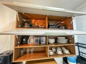 A kitchen with wooden shelves holding cookware, plates, and cups. - Condomíno American Praia (Porto Seguro)
