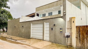 A two-story building with a garage door, a small balcony, and a security camera. - Condomíno American Praia (Porto Seguro)