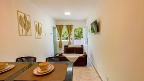 A hotel room with a dining area, a sofa, and a TV mounted on the wall. - Condomíno American Praia  (Porto Seguro)