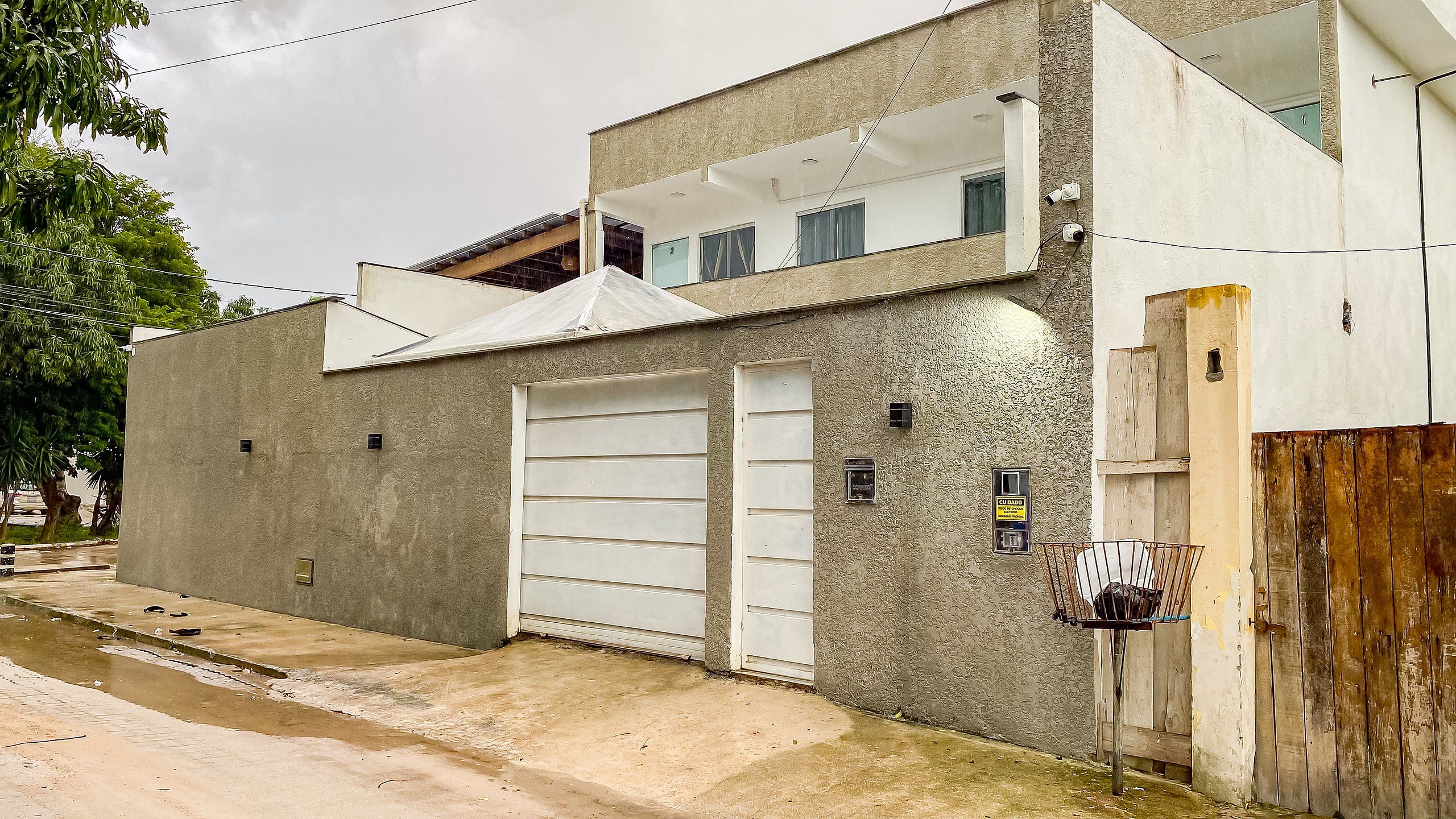 Um edifício de dois andares com porta de garagem, uma pequena varanda e uma câmera de segurança.