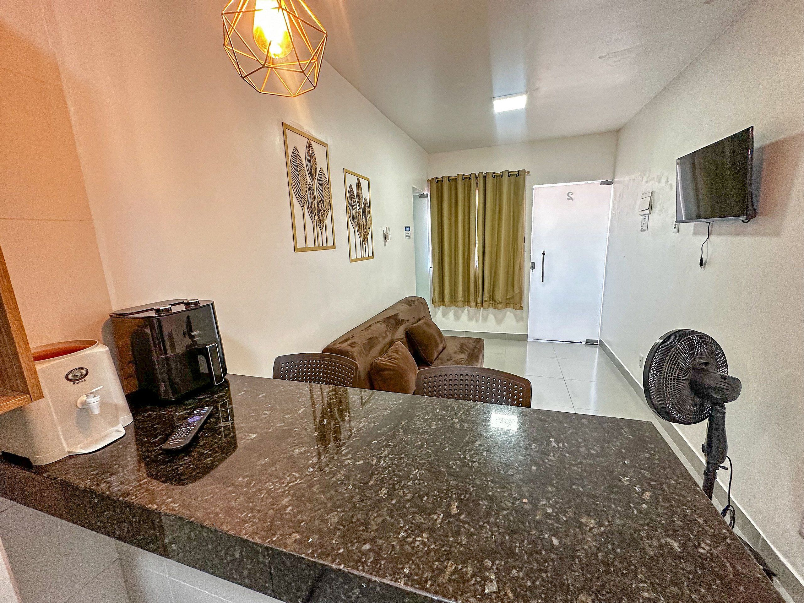 A kitchen area with a marble countertop, a coffee machine, a refrigerator, and a television mounted on the wall.