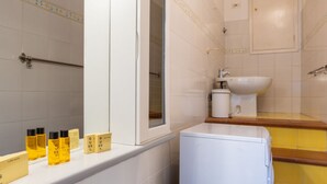Casa de banho com lavatório branco, espelho e artigos de higiene num prateleira.