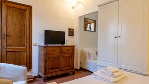 Quarto com guarda-roupa de madeira, televisão em um móvel, cama com roupa de cama branca e um quadro na parede.