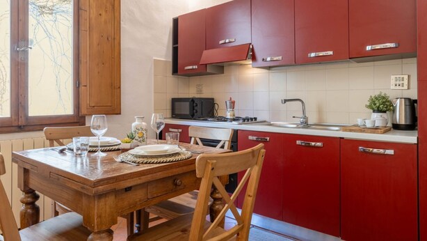 Uma cozinha com armários vermelhos, uma mesa de jantar de madeira e uma janela com vista para árvores.