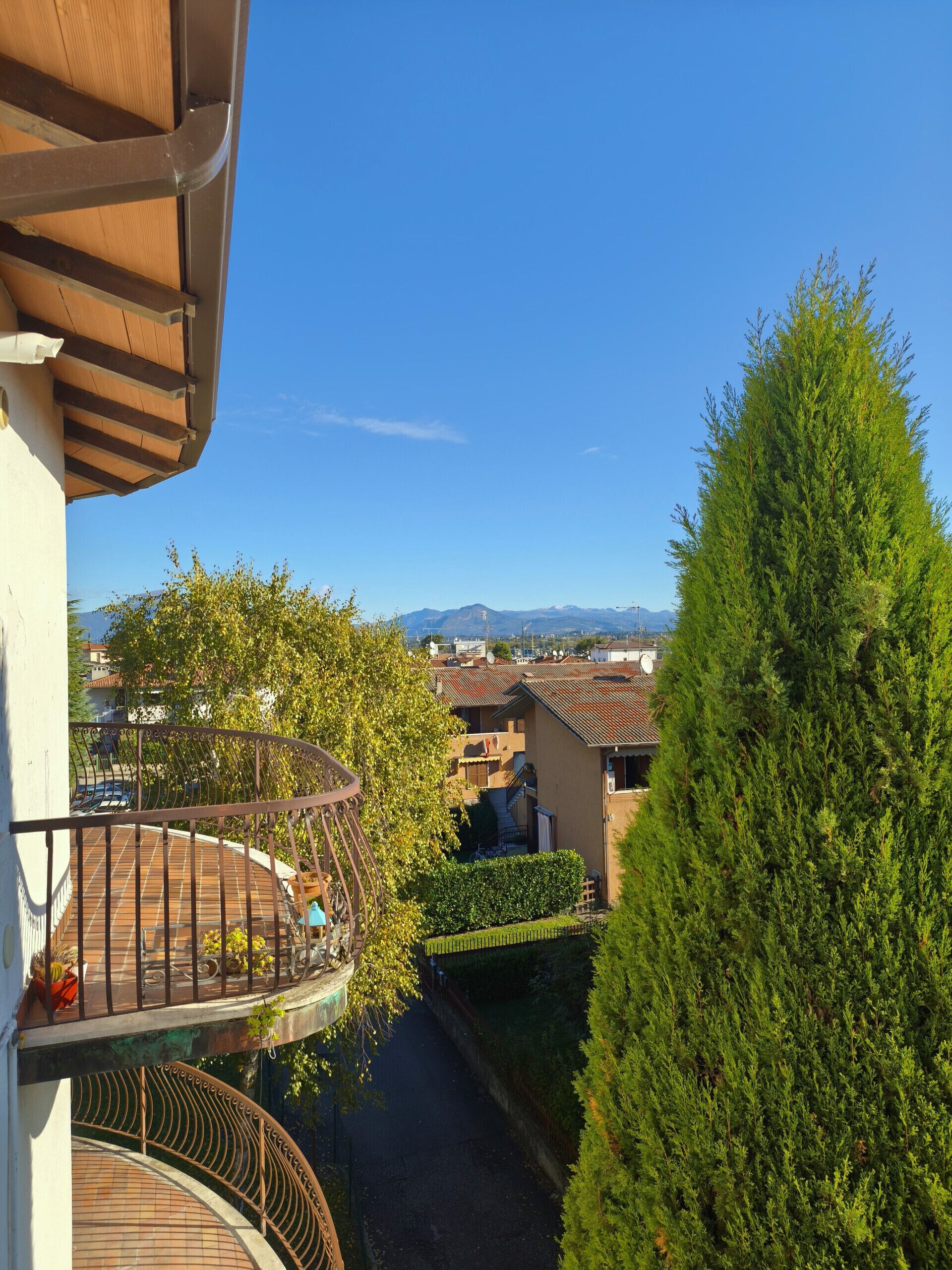 A residential balcony with a view of a tree and a distant mountain range.