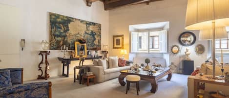 A spacious living room with a high ceiling, a large painting, a sofa, a coffee table, and a lamp.