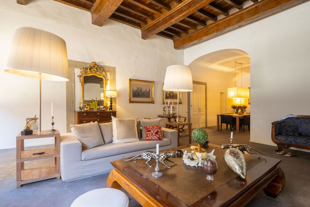 A cozy living room with a sofa, coffee table, and lamps. There is a dining area in the background with a table and chairs.