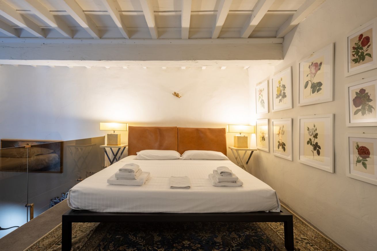 A hotel room with a large bed, two bedside lamps, a headboard, and a wall with framed floral artwork.